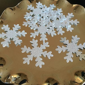 May include: A silver tray with a pile of silver glitter snowflake cutouts.