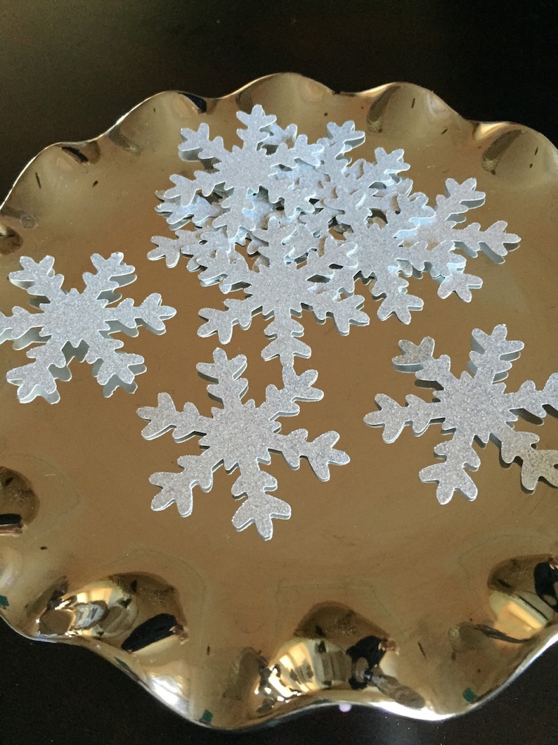 May include: A silver tray with a pile of silver glitter snowflake cutouts.