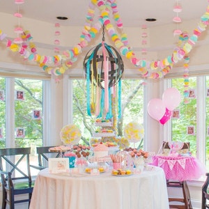 May include: A pink and white birthday party table setting with a cake, cupcakes, and other treats. The table is decorated with pink and white balloons, and a banner that says "One".