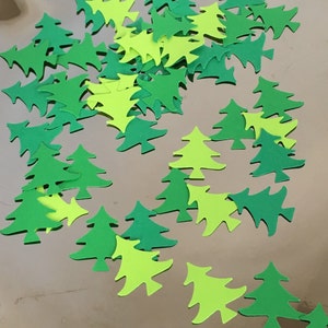 May include: A collection of green and lime green paper Christmas tree cutouts. The trees are scattered on a gold background.