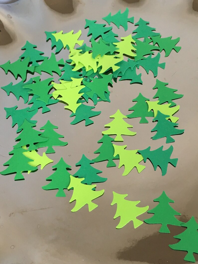 May include: A collection of green and lime green paper Christmas tree cutouts. The trees are scattered on a gold background.