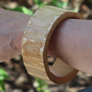Può includere: Un braccialetto in legno naturale di colore marrone chiaro, con una finitura liscia e lucida.