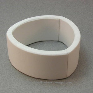 May include: A white, oval bracelet with a smooth, matte finish. The bracelet has a thick band and a rounded inner edge. The design is simple and modern, suitable for everyday wear. The bracelet is approximately 6.35 cm in diameter.