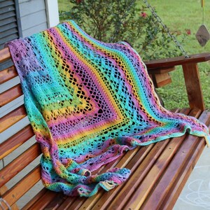 May include: A colorful crocheted throw blanket with a rainbow pattern draped over a wooden porch swing.