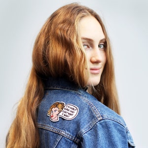 Peut inclure: Une femme aux longs cheveux ondulés brun rougeâtre porte une veste en jean bleue avec un patch au dos. Le patch représente une image de dessin animé d'une femme aux cheveux blonds et le texte "I'm Audrey Horne and I get what I want."
