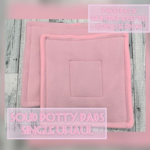 May include: Two square, solid light pink potty pads featuring a soft, fleece-like texture with stitched borders. The text on the image reads: TWO PACK MULTIPLE SIZES TO CHOOSE FROM and SOLID POTTY PADS SINGLE UHAUL.