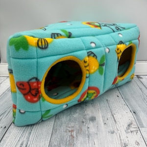 May include: A rectangular, light blue fleece pet tunnel featuring a colorful pattern of red, yellow, and green fish. The structure has two circular openings with yellow fabric trim, providing a soft, padded enclosure for small animals.