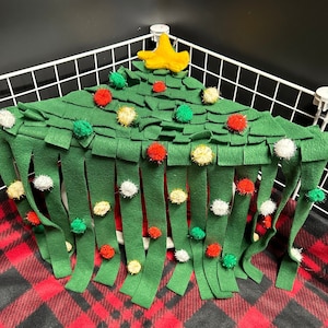 May include: A green felt Christmas tree with a yellow star on top. The tree has a fringe of green felt strips and is decorated with red, white, and yellow pom-poms.