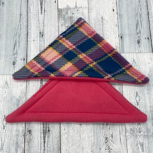 May include: Two triangular fabric pot holders made of fleece. The top pot holder features a multi-colored plaid pattern in shades of navy blue, pink, yellow, and purple. The bottom pot holder is a solid, vibrant pink color with stitched edges.
