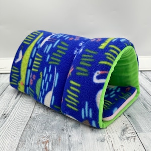May include: A blue fleece pet tunnel with a whimsical pattern of white birds, green plants, and pink flowers. The interior is bright green, and the entrance is lined with green fleece. A cozy hideaway for small pets.