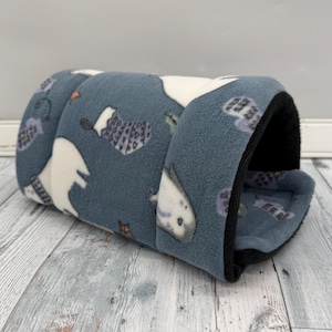 May include: A cylindrical pet tunnel made of soft blue fleece fabric featuring a repeating pattern of white polar bears and gray patterned stockings. The interior of the tunnel is lined with solid black fleece, creating a cozy, enclosed space.