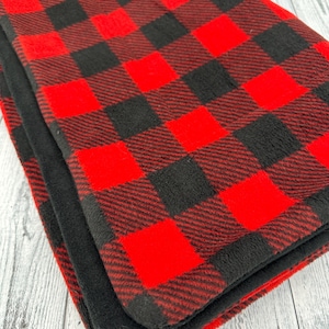 May include: Folded red and black buffalo plaid blanket. The blanket features a classic check pattern in bold red and black squares. The blanket is made of a soft, plush material, perfect for adding warmth and style to any space.