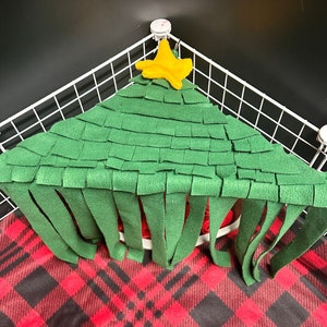 May include: A green felt Christmas tree with a yellow star on top. The tree has fringe around the bottom and is hanging in a white wire cage.