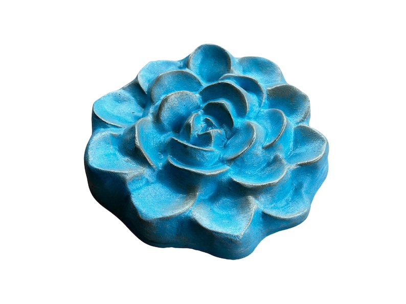 May include: A turquoise-colored, flower-shaped decorative object. The object has multiple layers of petals, with a textured surface and a slightly weathered appearance. The flower is a solid, three-dimensional piece, likely made of a durable material.