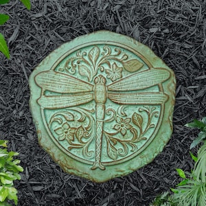 May include: A round, green stepping stone with a dragonfly design. The dragonfly is surrounded by floral details.