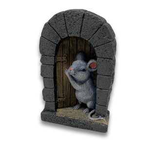 Op de afbeelding: Een grijs muisbeeldje dat uit een kleine, bruine houten deur kijkt die in een grijze stenen boog is geplaatst.