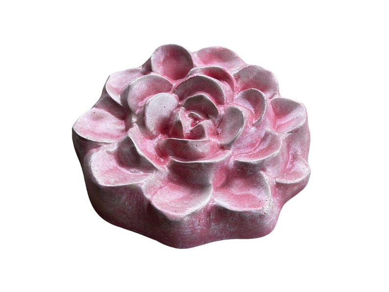 May include: A pink, flower-shaped decorative object. The object has multiple layers of petals, with a textured surface. The color is a soft pink with some areas of a lighter shade. The object is likely made of a solid material.