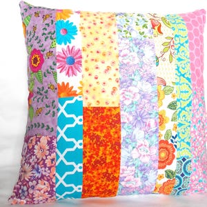 May include: A square throw pillow featuring a patchwork design of vertical fabric strips. The patterns include various floral prints, geometric shapes, and polka dots in vibrant colors such as purple, pink, orange, yellow, turquoise, and white.