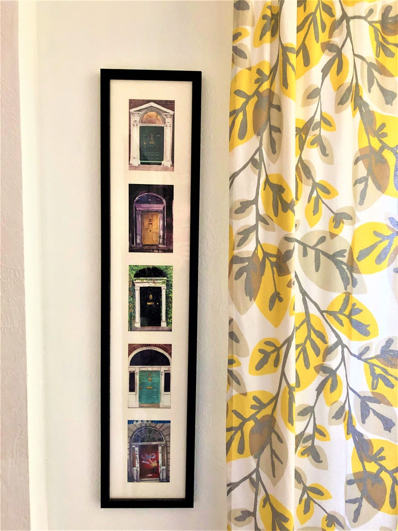 May include: A black framed picture with five photos of different doors. Each photo is in a white mount. The doors are all different colours and styles. The picture is hanging on a white wall next to a yellow and grey patterned curtain.