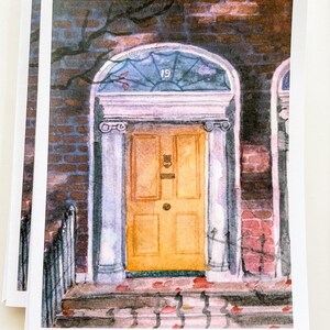 May include: A watercolor painting of a yellow door with a glass window above it. The door is framed by white columns and has a brass door knocker. The door is set in a brick wall with a vine growing up the side. The number "19" is visible on the glass window.
