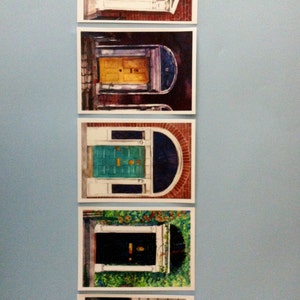 May include: Five framed watercolour paintings of colourful doors in various architectural styles. Each door is a different colour, including green, yellow, blue, black, and red.