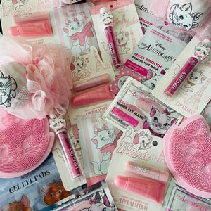 May include: A collection of Disney Aristocats Marie themed beauty products including pink bath sponges, lip gloss tubes with character toppers, lip balm duos, strawberry milk scented sheet masks, oat milk under eye masks, and pink silicone facial scrubbers.