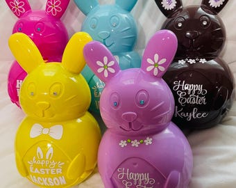 Könnte beinhalten: Fünf Osterei-förmige Sparschweine in verschiedenen Farben. Die Hasen sind rosa, blau, gelb, lila und braun. Jeder Hase hat einen anderen Namen: Jackson, Kaylee, Kasey und zwei weitere.