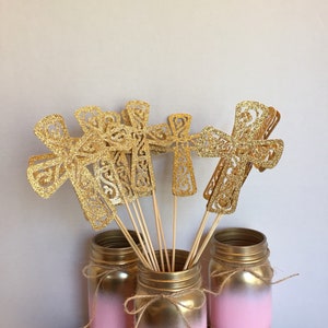 May include: Gold glitter cross cutouts on wooden sticks in pink ombre mason jars with twine bows.