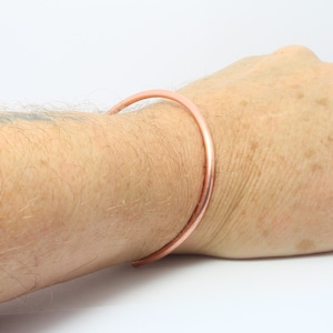 May include: A simple copper bangle bracelet worn on a person's wrist.
