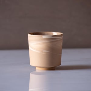 May include: A beige ceramic cup with a swirling white pattern. The cup has a rounded bottom and a slightly flared top.
