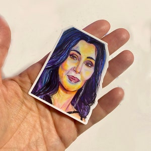 May include: A colorful watercolor painting of a woman with long dark hair, wearing a black top and earrings. The painting is done in a vibrant style with shades of purple, blue, yellow, and pink.