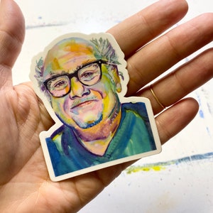 Peut inclure: Un autocollant en aquarelle coloré d'un homme avec des lunettes et une chemise bleue. L'autocollant est sur un fond blanc.