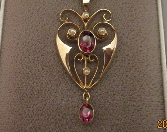 May include: A gold pendant necklace with a heart-shaped design featuring a large red gemstone and smaller white gemstones. The pendant has a delicate, intricate design with swirls and loops.