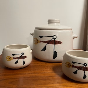 May include: A set of three white ceramic bowls with a brown, black, and yellow abstract design. The bowls are in different sizes and have a rounded shape.