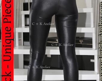 May include: Black, shiny leggings with a high waist and a sleek, form-fitting design. The leggings are paired with black platform heels. The image includes text that reads "Einzelstück - Unique Piece" and "C + K Atelier".