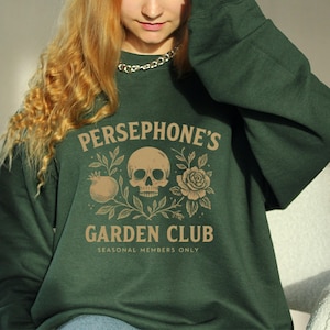 Sweatshirt featuring skull, pomegranate, and floral elements with text “Persephone’s Garden Club