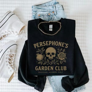 Sweatshirt featuring skull, pomegranate, and floral elements with text “Persephone’s Garden Club
