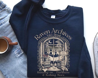 Puede incluir: Sudadera azul marino con un gráfico de una escena de ventana con el texto "Raven Archives Vol. 1 - Dread". La ventana muestra un paisaje urbano, libros y el texto "Entry Forbidden". La frase "Running on....Darkness & Nothing More." está en la parte inferior.