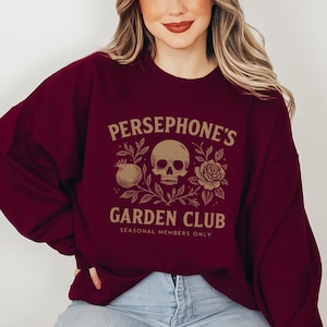 Sweatshirt featuring skull, pomegranate, and floral elements with text “Persephone’s Garden Club