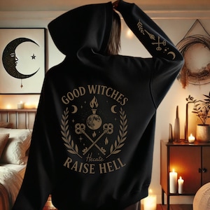 May include: Black hooded sweatshirt with the text "Good Witches Raise Hell" in a circular design on the back. The design includes a moon, keys, and other mystical symbols. The sleeve features an arrow, keys, and crescent moon design.