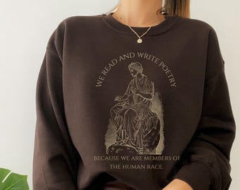 May include: A dark brown sweatshirt with the text "WE READ AND WRITE POETRY" arched around a seated figure illustration. Below the illustration is the text "BECAUSE WE ARE MEMBERS OF THE HUMAN RACE."