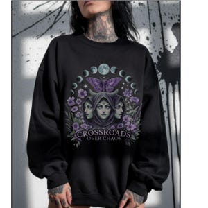 Crossroads Over Chaos sweatshirt featuring a moon goddess design, triple moon phase, violet flowers, butterfly, and the empowering phrase "Crossroads Over Chaos." Available in black, navy, maroon, and heather grey. Perfect for witchy aesthetic lovers and celestial symbolism fans.
