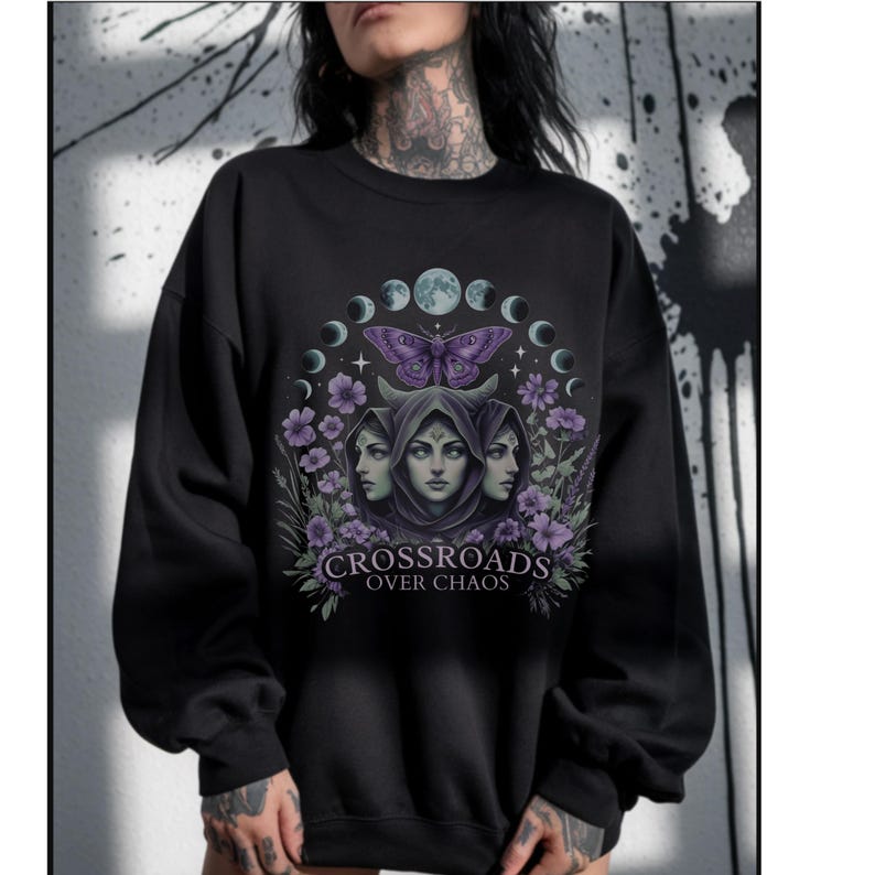 Crossroads Over Chaos sweatshirt featuring a moon goddess design, triple moon phase, violet flowers, butterfly, and the empowering phrase "Crossroads Over Chaos." Available in black, navy, maroon, and heather grey. Perfect for witchy aesthetic lovers and celestial symbolism fans.