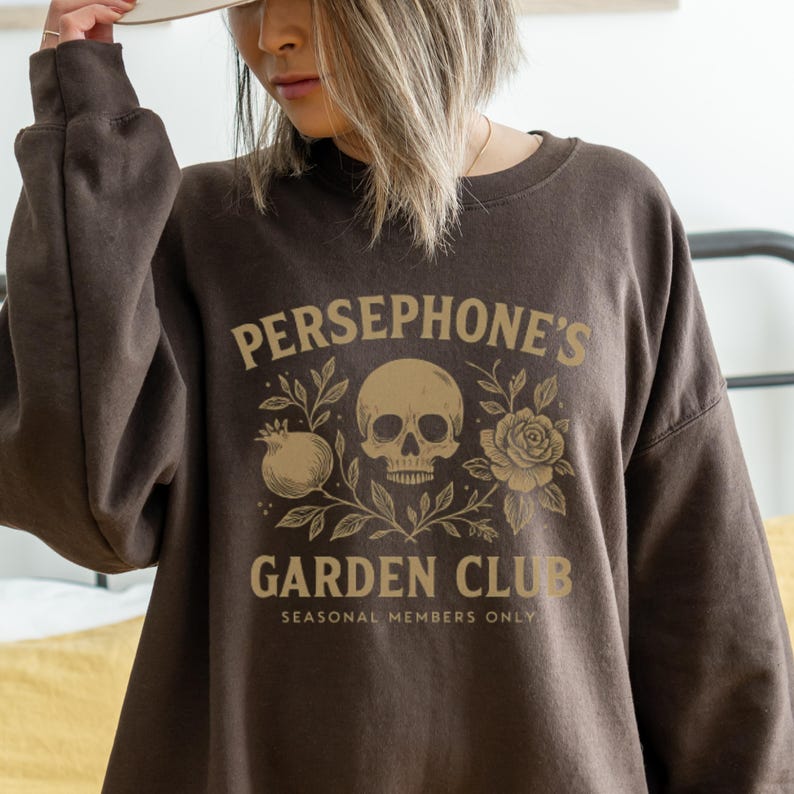 Sweatshirt featuring skull, pomegranate, and floral elements with text “Persephone’s Garden Club