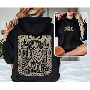 Black hoodie with linocut-style howling wolf and moon phases design on back.