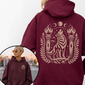 Hoodie with beige howling wolf and triple moon design. Navy hoodie with same design. Maroon hoodie with back wolf design and small front paw print. Black and dark chocolate hoodies shown on models, with front and back views.