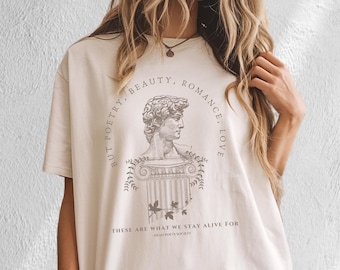 Könnte beinhalten: Beige T-Shirt mit einer klassischen Büstenillustration und den Worten "BUT POETRY, BEAUTY, ROMANCE, LOVE" und "THESE ARE WHAT WE STAY ALIVE FOR - DEAD POETS SOCIETY" in Schwarz gedruckt.