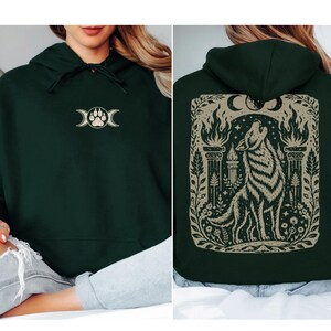 Model wearing forest green hoodie with large wolf illustration on the back.