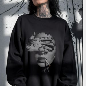 Woman wearing an oversized black Lilith sweatshirt featuring a grayscale “Not From the Rib” feminist graphic, styled with layered silver necklaces and dark alternative clothing.