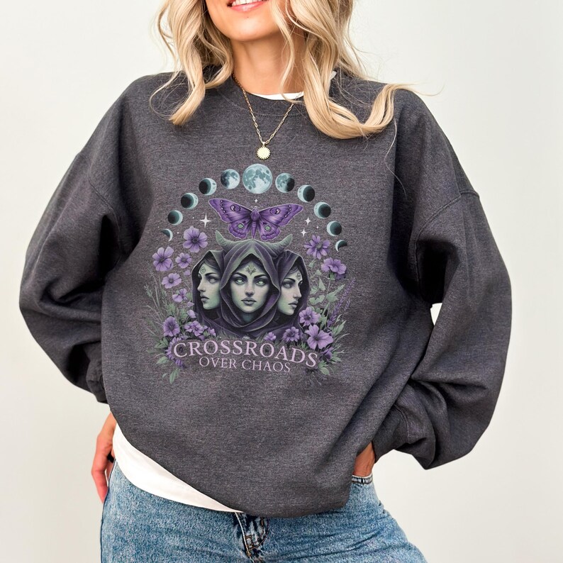 Crossroads Over Chaos sweatshirt featuring a moon goddess design, triple moon phase, violet flowers, butterfly, and the empowering phrase "Crossroads Over Chaos." Available in black, navy, maroon, and heather grey. Perfect for witchy aesthetic lovers and celestial symbolism fans.